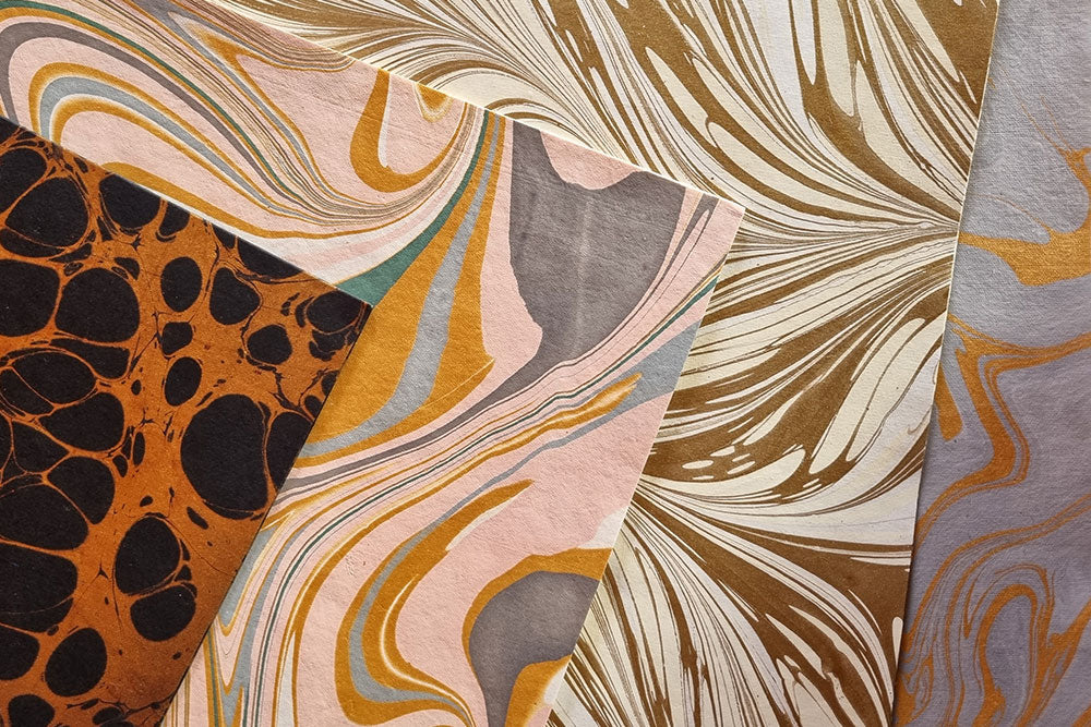 Four marbled paper gift wrap sheets layered on top of each other to show the different designs